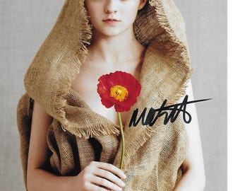 May include: A portrait featuring a person wearing a burlap hood and top, holding a red flower with a yellow center. The image has a neutral background and a signature in black ink.