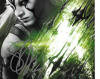 May include: A portrait of a character with pale skin, white hair, and striking black markings on the face. The character has intense yellow eyes and is set against a backdrop of green and black abstract shapes, possibly a science fiction or fantasy theme.