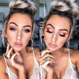 May include: A woman with light brown hair styled in a bun, wearing a white lace top, has on natural makeup with a peachy eyeshadow and a nude lip color. She is wearing a gold necklace with a small oval pendant.