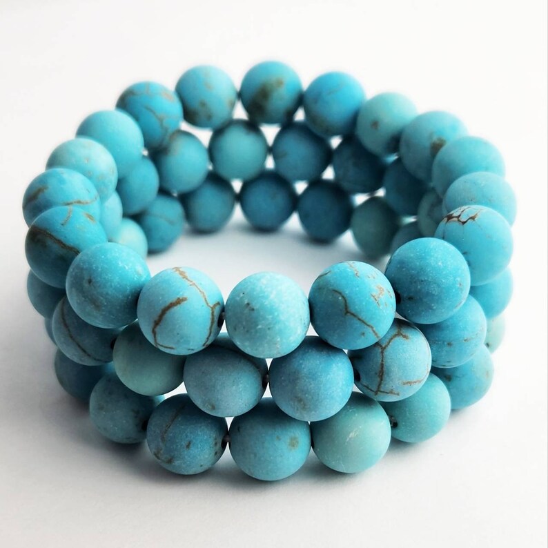 Puede incluir: Una pulsera de varias vueltas compuesta por cuentas redondas y mate de color turquesa. Cada cuenta presenta patrones de vetas marrones de aspecto natural en toda su superficie. Las cuentas est&aacute;n ensartadas en c&iacute;rculo, creando un aspecto superpuesto.