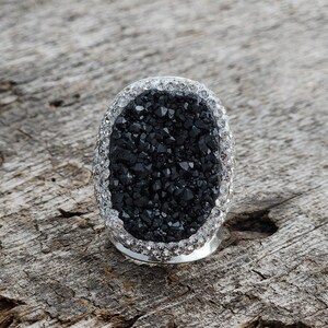 May include: A black oval ring with a sparkly silver band. The ring is made of a black stone with a rough, textured surface.