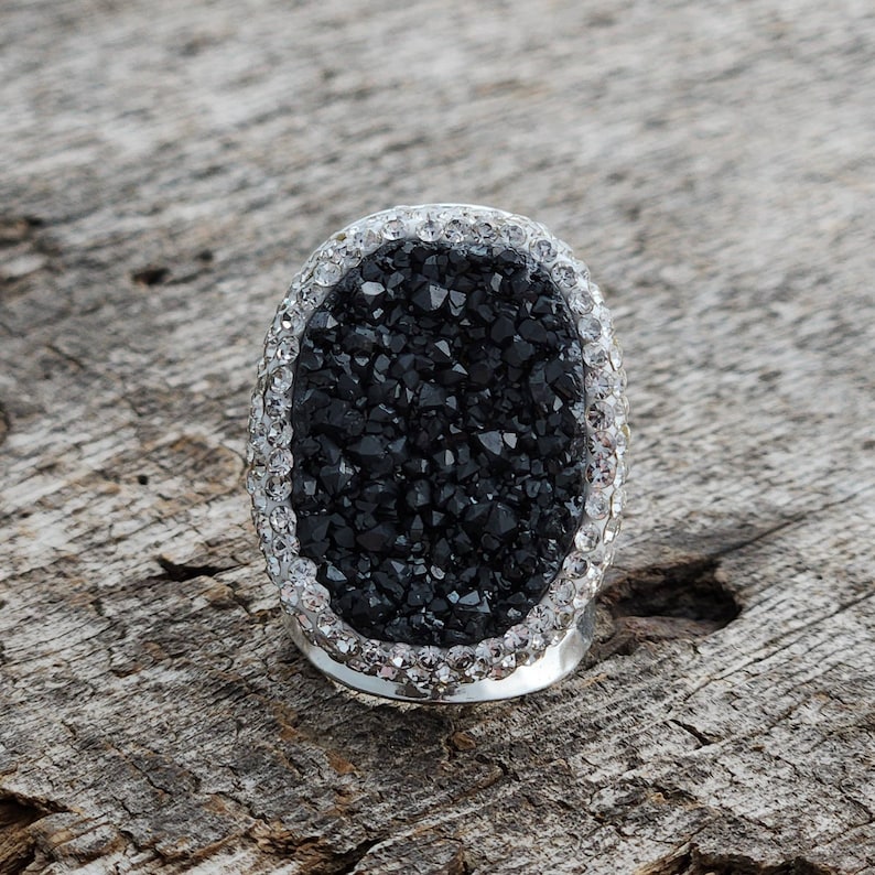 May include: A black oval ring with a sparkly silver band. The ring is made of a black stone with a rough, textured surface.