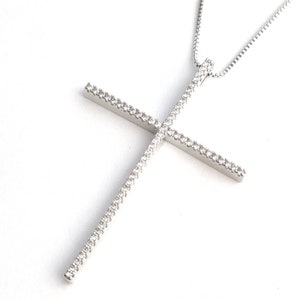 May include: A silver necklace with a large, sparkling cross pendant. The cross is made of silver and is encrusted with small, clear stones.