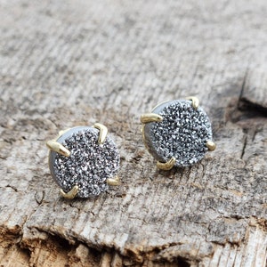 May include: A pair of silver and gold stud earrings with a sparkly, textured finish.