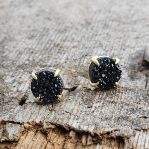 May include: A pair of black stud earrings with gold settings. The earrings are made of black crystal and have a round shape.