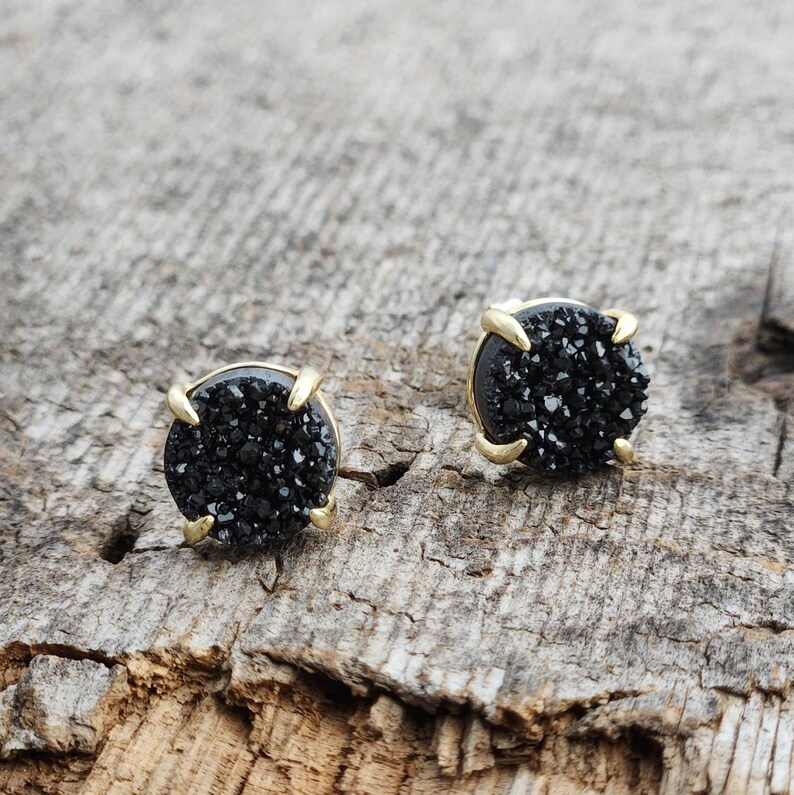 May include: A pair of black stud earrings with gold settings. The earrings are made of black crystal and have a round shape.
