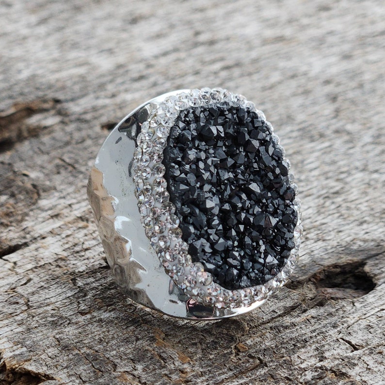May include: A silver ring with a black oval-shaped stone surrounded by clear rhinestones.