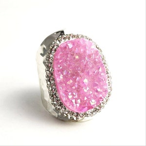 May include: A silver ring with a large pink crystal set in a silver bezel. The crystal is surrounded by a row of small clear rhinestones.