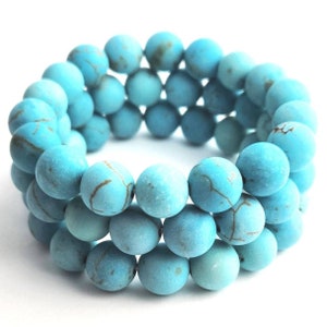 Puede incluir: Una pulsera de tres hileras compuesta por cuentas redondas de acabado mate en color turquesa. Cada cuenta presenta un patr&oacute;n veteado de color marr&oacute;n oscuro en su superficie, lo que crea una apariencia texturizada en toda la pieza circular.
