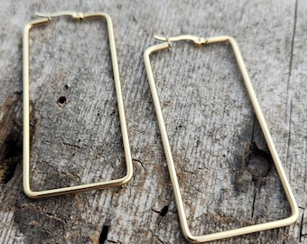 May include: A pair of gold-toned rectangular hoop earrings. The earrings are made of a thin metal and have a simple, modern design.