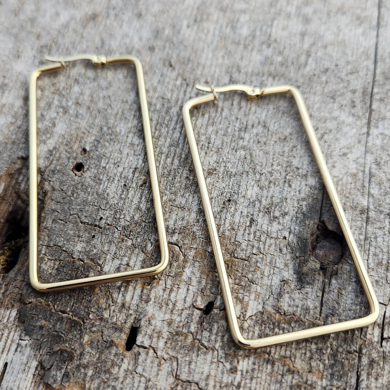K&ouml;nnte beinhalten: Ein Paar goldfarbene rechteckige Creolen. Die Ohrringe sind aus d&uuml;nnem Metall gefertigt und haben ein schlichtes, modernes Design.