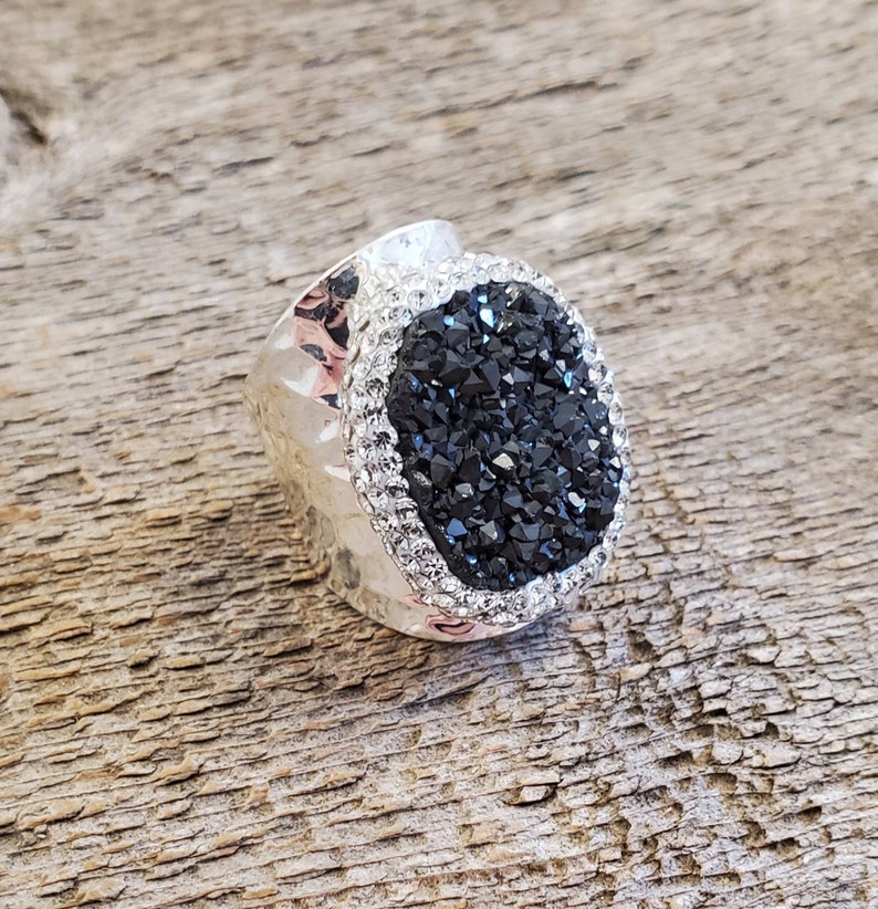 May include: A silver ring with a black gemstone surrounded by clear rhinestones.