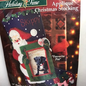 May include: A felt Christmas stocking with a Santa Claus applique, a picture frame for a pet photo, and the words "Skippy" and "Favorite Pet". The stocking is 18 inches in diameter.