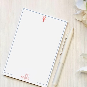 May include: A white notepad with a blue border and a red lobster illustration. The notepad has the name "nikki" written in red at the bottom.