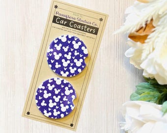May include: Two car coasters with a dark blue background and a white Mickey Mouse pattern. The coasters are displayed on a cardboard backing with the text "Car Coasters" and "Passiflora Studios Co."