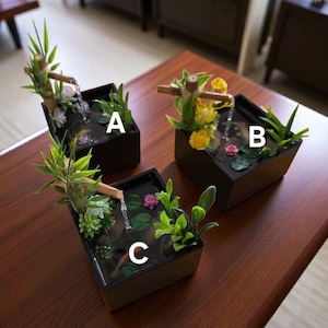 以下が含まれることがあります： 竹の水場と小さな植物を備えた3つのミニチュア禅ガーデンファウンテン。各噴水は黒い長方形の容器に入っています。1つは黄色の花、もう1つは紫色のスイレン、3つ目は緑の植物があります。