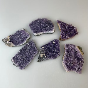 Può includere: Sei gruppi di cristalli di ametista, ognuno con una forma e una dimensione uniche, che mettono in mostra la bellezza naturale della pietra preziosa viola.