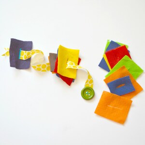 May include: A set of felt squares with slits cut in them, a yellow ribbon with white polka dots, and a green button. The felt squares are in various colors, including red, orange, yellow, green, blue, and purple.
