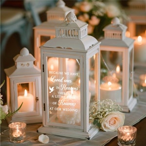 May include: White lantern with a glass panel featuring the text "Because we have loved ones in Heaven, there's a little piece of Heaven at our wedding". The lantern has a white dove graphic and is lit with a candle inside.