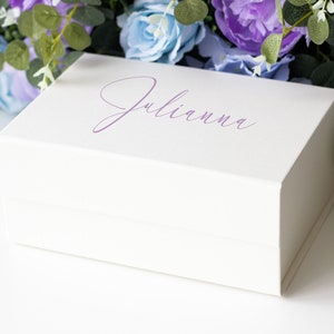 Può includere: Una scatola regalo bianca con una scritta viola che dice "Julianna".