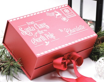 May include: A red gift box with a white ribbon and a white label that says "From Santa Claus - the North Pole to Charlotte".