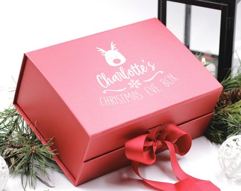 May include: A red Christmas Eve box with a matching red ribbon tied in a bow. The box has a white reindeer graphic and the text "Charlotte's Christmas Eve Box". The box is surrounded by Christmas decorations.