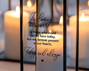 May include: Two black metal candle lanterns with glass panels. The lanterns are filled with white candles and have a quote that reads "In loving memory of those who could not be here today, but are forever present in our hearts, Today and always".