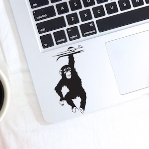 May include: A black and white sticker of a monkey hanging from a branch on a silver laptop.