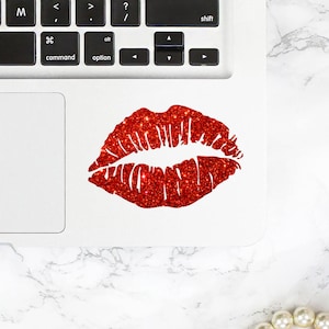 May include: A white laptop computer with a red glitter lip print sticker on the trackpad.