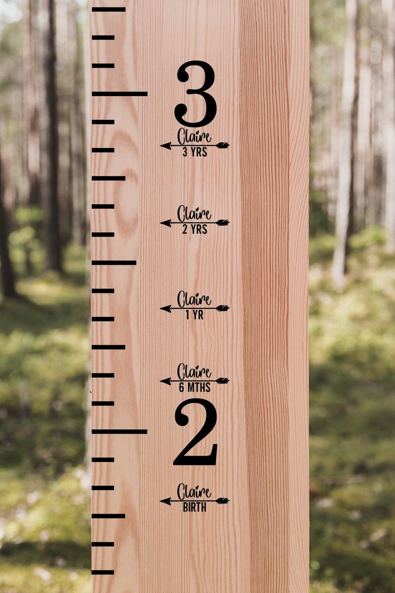 Op de afbeelding: Een houten groeimeter met zwarte markeringen en tekst. De meter toont de lengte van een kind genaamd Claire op verschillende leeftijden, waaronder geboorte, 6 maanden, 1 jaar, 2 jaar en 3 jaar.