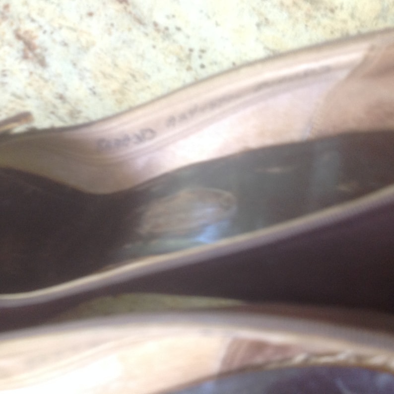 May include: A pair of brown leather ballet flats with a light brown sole. The flats have a small, round, brown leather patch on the inside of the shoe.