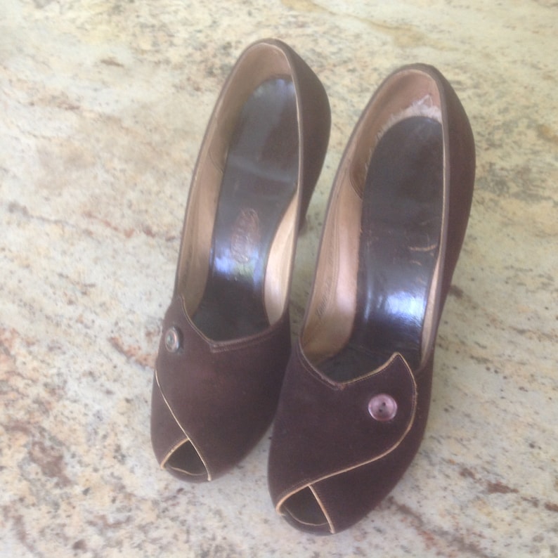 May include: A pair of brown suede peep-toe heels with a button detail on each shoe.