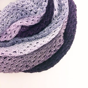 Puede incluir: Una bufanda infinita de ganchillo con un degradado de colores púrpura, lavanda y gris.