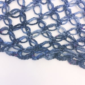 Pode incluir: Um close-up de um tecido de crochê azul com um degradê de cor do azul escuro para o azul claro. O tecido é feito com um padrão de ponto simples e tem uma sensação delicada e arejada.