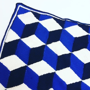May include: A blue and white crocheted blanket with a geometric pattern. The blanket is made with a 3D effect, creating a unique and modern look.