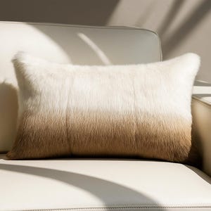 Könnte beinhalten: Ein rechteckiges Zierkissen mit Farbverlauf. Der obere Teil ist weiß, der untere Teil ist braun. Das Kissen besteht aus weichem, fellartigem Material und liegt auf einem weißen Ledersofa.