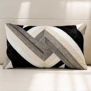 Könnte beinhalten: Rechteckiges Zierkissen mit geometrischem Muster. Das Kissen hat ein Patchwork-Design mit abwechselnden Streifen in Schwarz, Weiß und verschiedenen Grautönen. Das Kissen besteht aus einem strukturierten Material und liegt auf einer hellen Oberfläche.