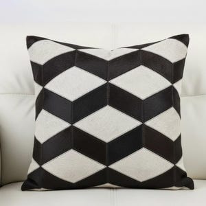 Könnte beinhalten: Quadratisches Zierkissen mit geometrischem Muster. Das Kissen zeigt ein sich wiederholendes Design aus schwarzen und weißen Rauten, das einen auffälligen visuellen Effekt erzeugt. Das Kissen besteht wahrscheinlich aus einem weichen, strukturierten Material.