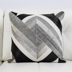 Könnte beinhalten: Quadratisches Zierkissen mit einem geometrischen Muster in Schwarz, Weiß und Grautönen. Das Kissen hat ein Patchwork-Design mit einem pfeilartigen Streifenmuster. Das Kissen liegt auf einer weißen Oberfläche. Maße: ca. 40 cm x 40 cm.