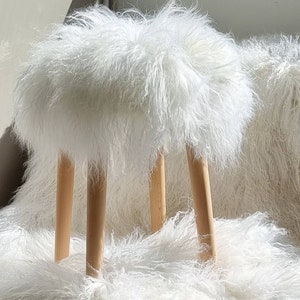 May include: White faux fur stool with four wooden legs. The stool is sitting on a white faux fur rug.