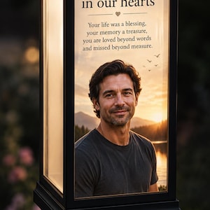May include: A black solar-powered memorial lantern featuring a portrait of a man against a sunset landscape. The text reads: Forever in our hearts. Your life was a blessing, your memory a treasure, you are loved beyond words and missed beyond measure.