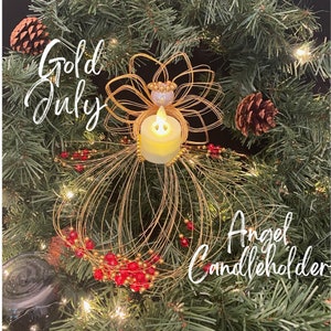 May include: A gold wire angel candleholder with a faux candle, red beads, and the text "Gold July Angel Candleholder" on a background of evergreen branches and pinecones.
