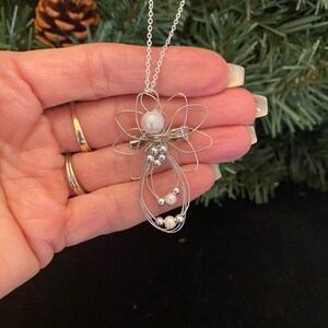 Hand view of 1.5-inch Handcrafted Silver Wire Angel Necklace - accented with silver and white beads. Elegant Heavenly Charm - Unique Gift for Her