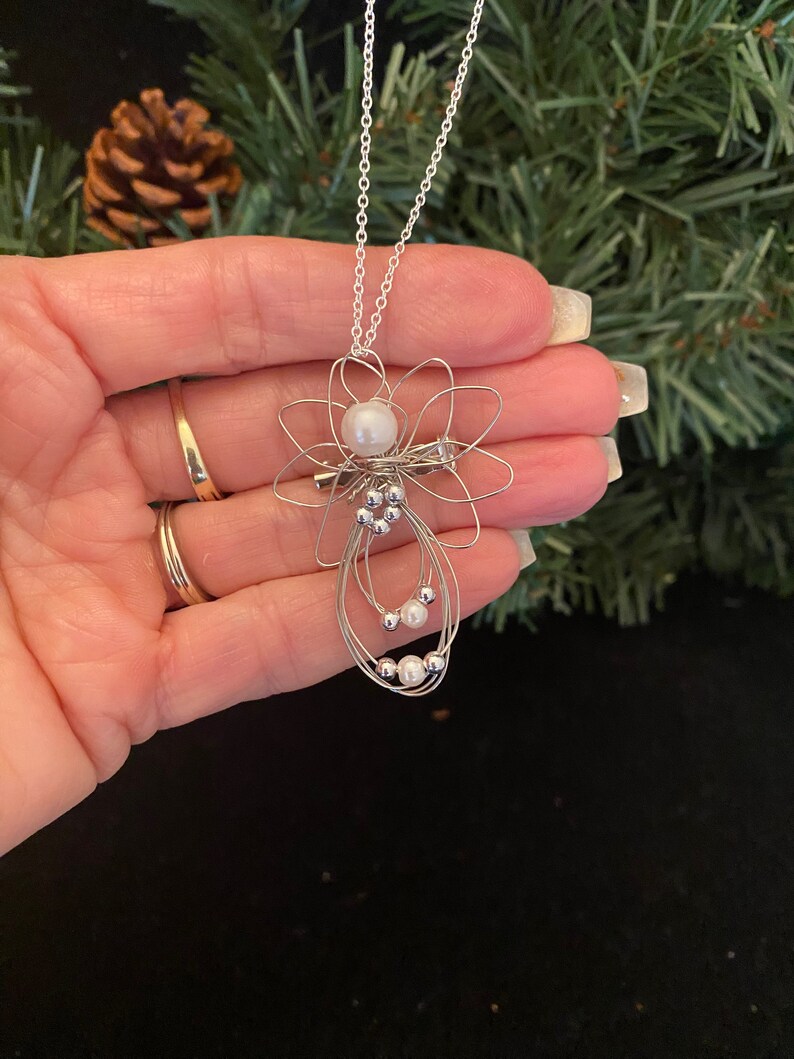 Hand view of 1.5-inch Handcrafted Silver Wire Angel Necklace - accented with silver and white beads. Elegant Heavenly Charm - Unique Gift for Her