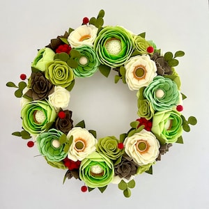 Corona navideña de fieltro hecha a mano con decoración floral en tonos verde crema.