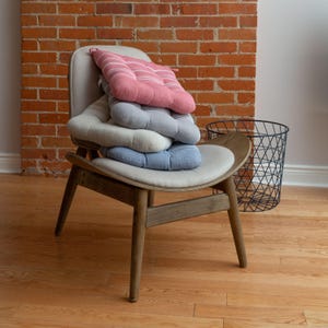 May include: A stack of four striped chair cushions in pink, gray, beige, and blue on a wooden chair with a brown wooden frame.