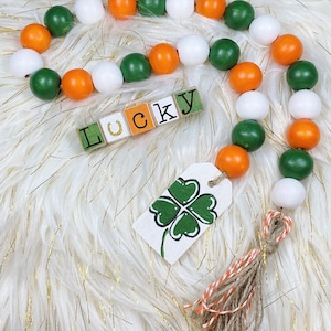 May include: A green, white, and orange beaded garland with a four-leaf clover charm and a wooden sign that says "Lucky".