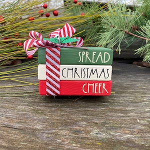 May include: A stack of three wooden blocks painted in red, white, and green with the words "Spread Christmas Cheer" written in black. The blocks are decorated with a red and white striped ribbon.