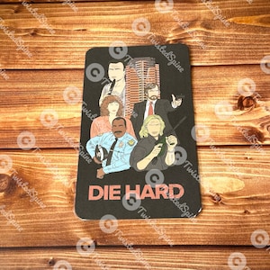 May include: Black rectangular graphic featuring a group of characters from the film "Die Hard". The characters are in a cartoon style, with the film title in red block letters at the bottom. The background is a wooden surface.