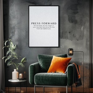 May include: A framed print with the text "PRESS FORWARD" in a modern font. Below the title is a motivational quote. The print hangs above a green velvet armchair with an orange pillow. A black floor lamp and a small side table are also visible.